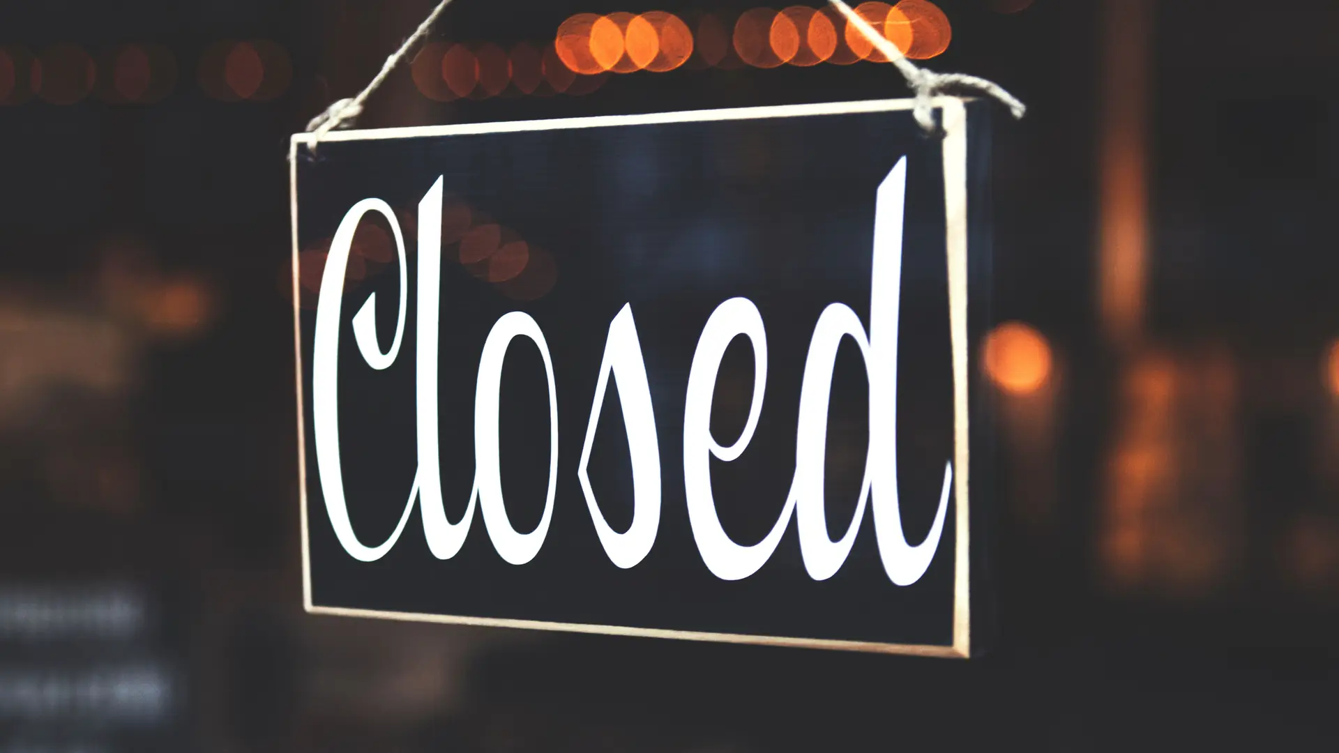 Closed sign hanging in a shop window with warm lights behind it