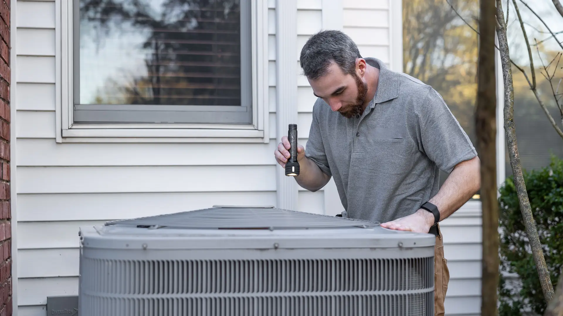 HVAC technician inspecting an outdoor air conditioning unit at a home